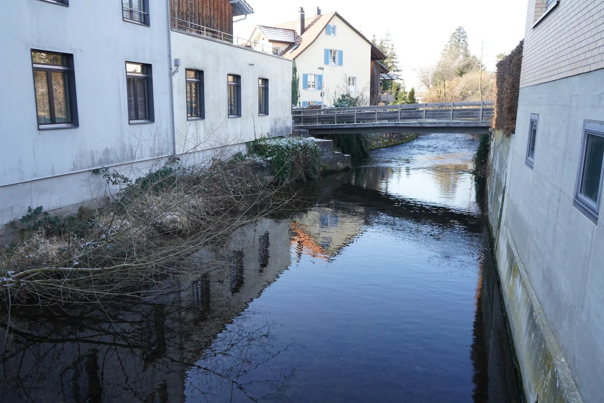 Ein kanalisierter Bach fliesst zwischen Gebäuden hindurch.